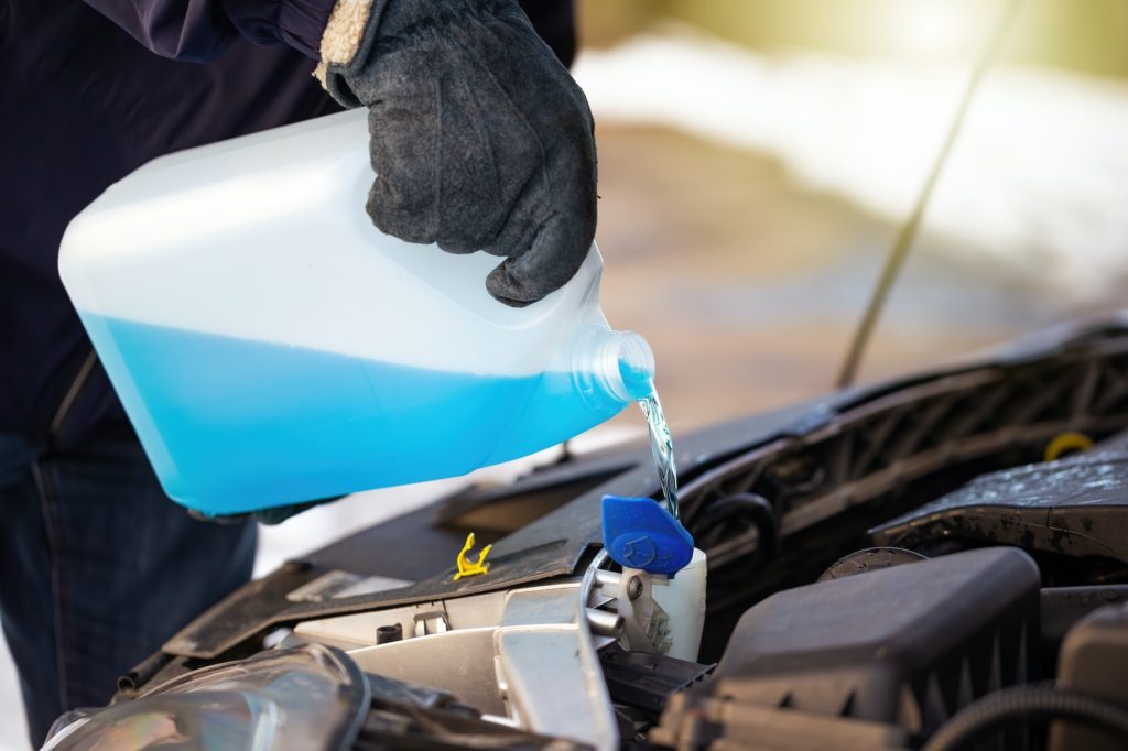 Man filling antifreeze coolant for cleaning front window with snow in background